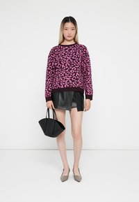 Maglione leopardato rosa e nero con polsini a costine, abbinato a una mini gonna in pelle nera e a una piccola borsa nera. Décolleté grigie a punta.