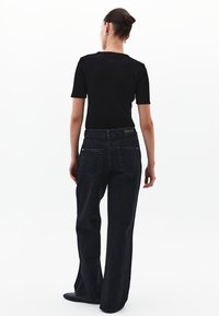 Top corto negro de canalé de manga corta, combinado con jeans de mezclilla oscura de cintura alta, que cuentan con bolsillos traseros y una etiqueta en la cinturilla.