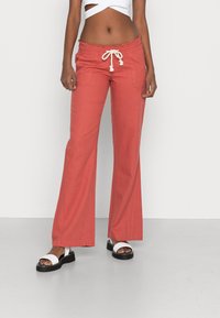 Red, flared pants with an elastic waistband and drawstring. Worn with a white cropped top and black platform sandals. Simple pockets visible.