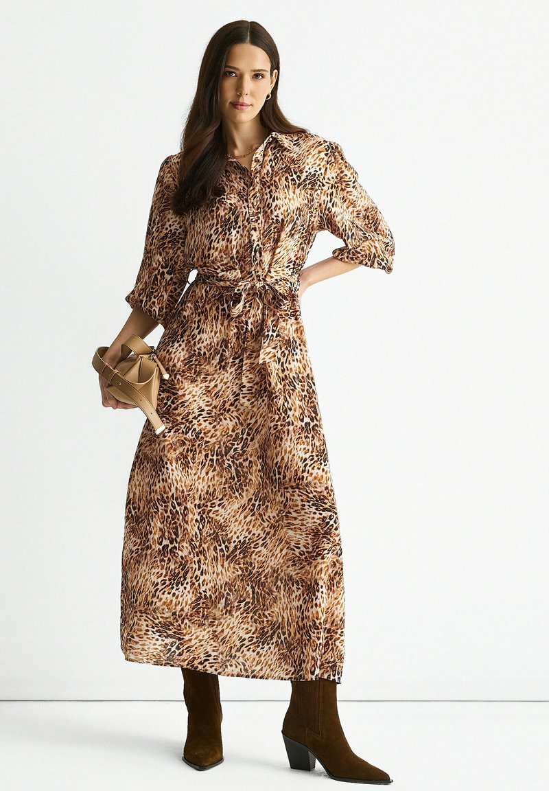 Leopard print maxi dress with a tied waist, button-down front, three-quarter sleeves, and a soft, flowy fabric; paired with brown heeled boots.