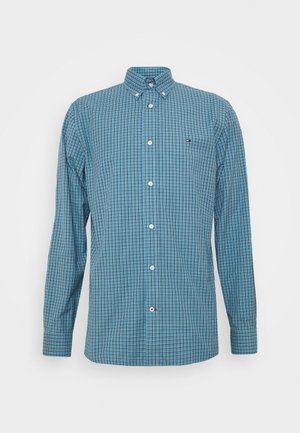 Chemise à manches longues boutonnée bleue avec motif à carreaux noir et blanc et petit logo sur le côté gauche de la poitrine.