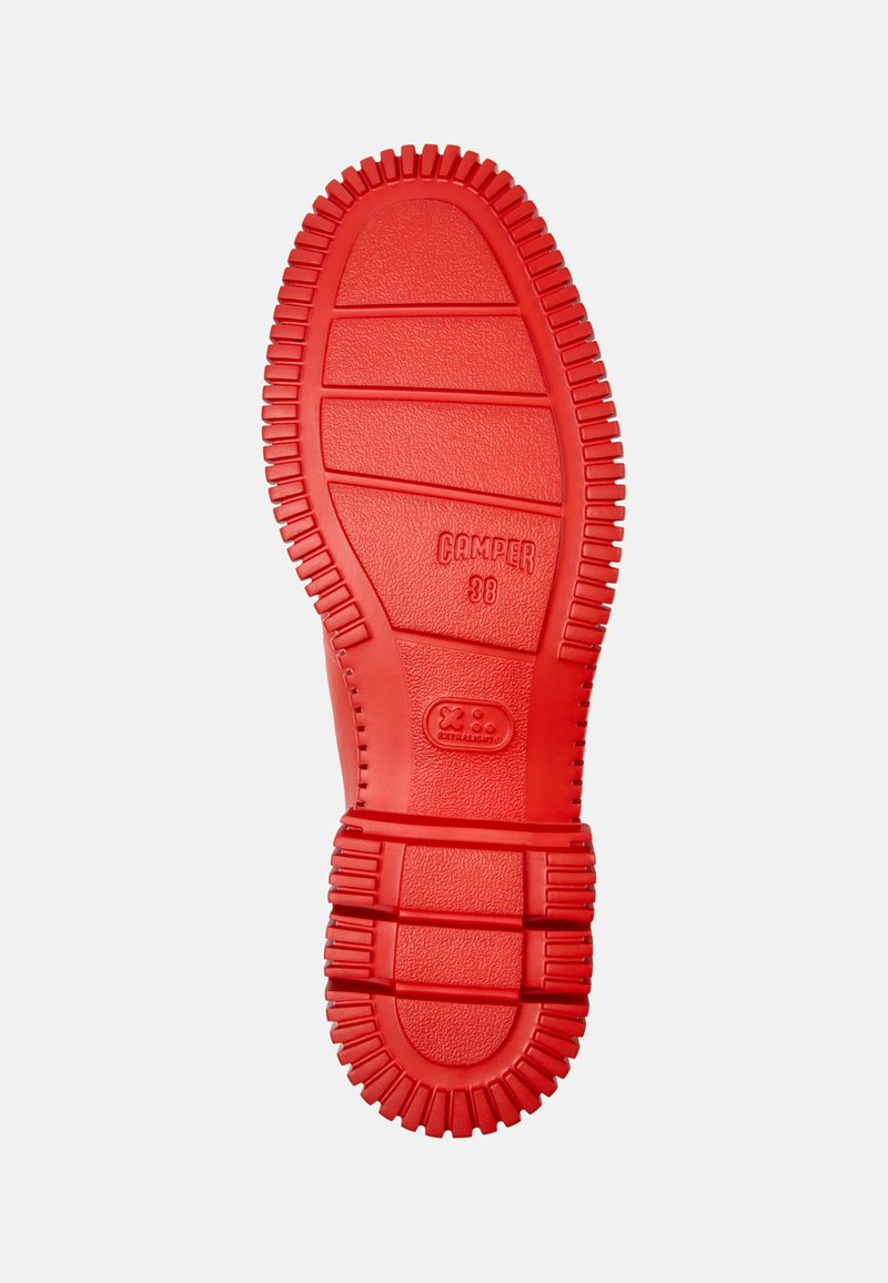Suela de zapato de goma roja con un patrón estriado y ranuras. Presenta la marca CAMPR, lo que proporciona tracción y durabilidad. Diseño plano, superficie texturizada.
