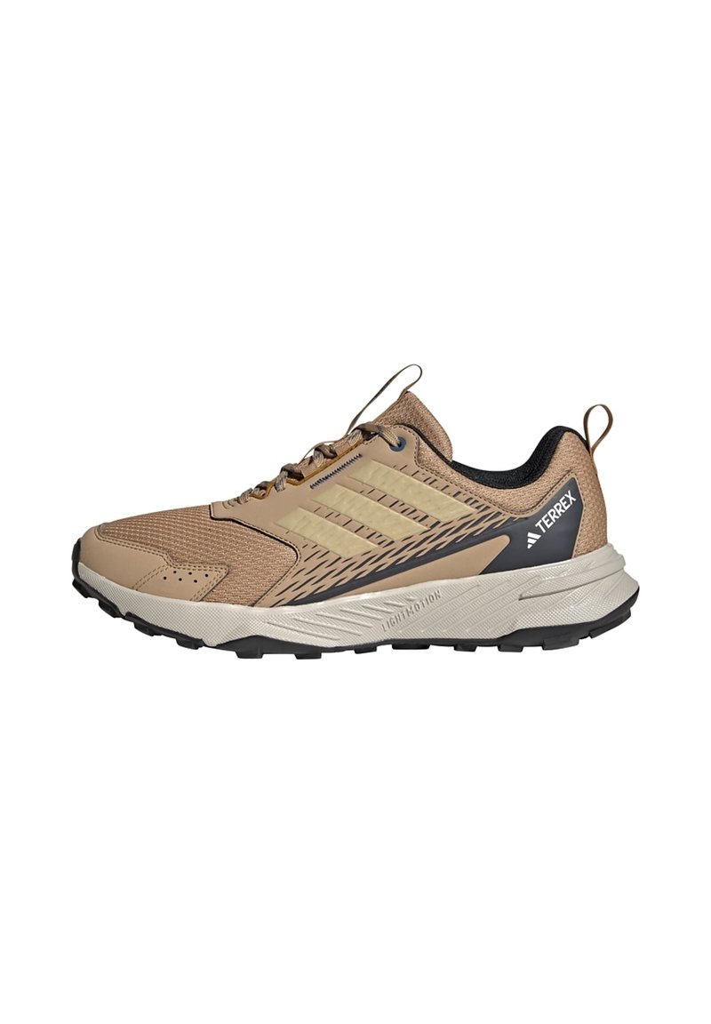 Beige træningssko med mesh-overdel, syntetiske overlays, sorte accenter, gummisål og tekstureret grebmønster. Letvægtsdesign med polstring.