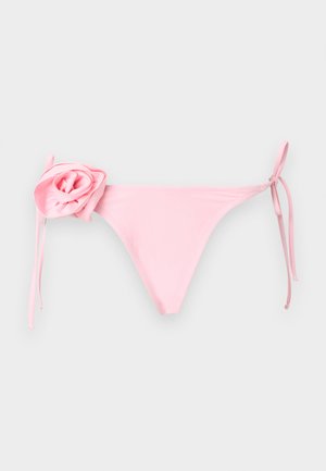 Bas de bikini rose clair avec liens latéraux réglables et une grande décoration en forme de rose en tissu sur la hanche gauche, sur un fond uni.