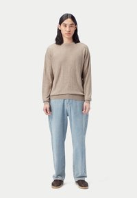 Beige texturerad tröja, löst sittande ljusblå jeans och bruna vävda slip-on skor. Outfiten har en avslappnad passform med en mjuk textur.