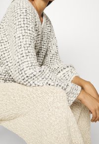 Strickpullover in Creme mit grauen Sprenkeln, mit V-Ausschnitt und langen Ärmeln. Weiches, strukturiertes Garn sorgt für ein gemütliches Erscheinungsbild.