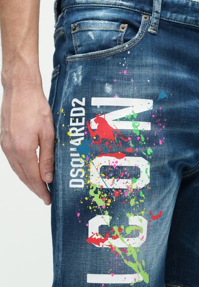 Jean en denim avec une texture usée et des accents de tâches de peinture colorées. Logo "DSQUARED2" imprimé en blanc sur le côté.