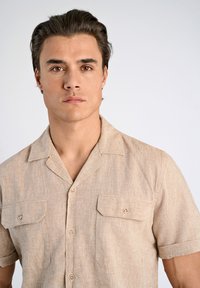 Korte mouwen shirt in lichtbeige stof, met een gestructureerde afwerking, twee voorzakken en een klassieke kraag met knoopsluitingen.