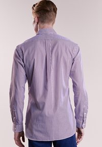 Herrskjorta med lång ärm i lila och vita ränder. Har en spetskrage, knappar vid ärmslut och en svängd nederkant. Tillverkad av bomull.