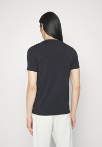 T-shirt corto blu scuro a maniche corte in un tessuto lucido con collo giro classico, visto da dietro, abbinato a pantaloni chiari.