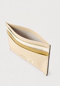 Δερμάτινη θήκη καρτών με τρεις θήκες σε μπεζ, κρεμ και χρυσό. Υφή εξωτερικά με λείο εσωτερικό επένδυση. Μινιμαλιστικός σχεδιασμός.