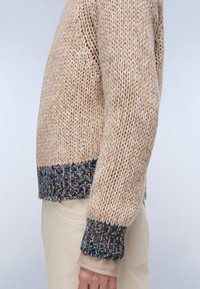 Beżowy sweter dziany z teksturowanym wzorem. Posiada wielokolorowy, prążkowany dół i mankiety z niebieskimi, brązowymi i kremowymi akcentami.