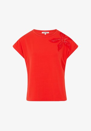 Punainen lyhythihainen t-paita, joka on valmistettu puuvillasta ja jossa on koristeellinen brodeerattu kukka vasemmassa olkapäässä helmikoristeilla.