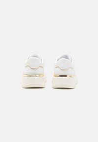 Sneakers bianchi con tomaia in pelle liscia, dettaglio dorato sul tallone e suola spessa e imbottita per il comfort. Dettagli ondulati sul retro.