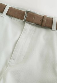 Gros plan sur un pantalon beige texturé avec une ceinture en daim marron clair dotée d'une boucle carrée en argent.