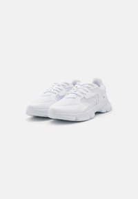 Zapatillas deportivas blancas con paneles de malla, lengüetas acolchadas, suelas de goma y diseño de cordones; presenta un sutil logotipo de la marca en el costado.