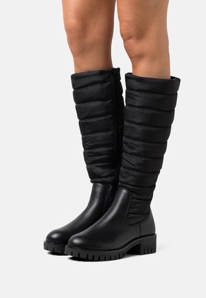 Bottes noires montantes jusqu'au genou, avec une partie inférieure lisse et imperméable et une partie supérieure matelassée rembourrée, dotées d'une fermeture éclair latérale et d'une semelle texturée.