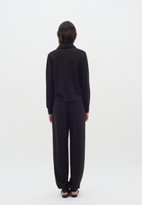 Musta loungewear-setti, joka koostuu pitkähih from yläosasta ja löysistä housuista. Valmistettu sileästä kankaasta, jossa on minimalistinen muotoilu ja ilman näkyviä kuvioita.