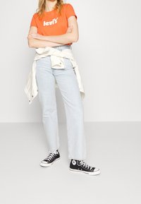 Camiseta de algodón naranja con el logo de "Levi's", vaqueros rectos de color azul claro y zapatillas altas negras con acentos blancos.