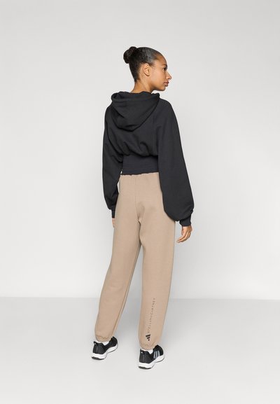 Μαύρο κοντό φούτερ με κουκούλα και φουσκωτά μανίκια συνδυασμένο με μπεζ φόρμα παντελονιού με λογότυπο, και τα δύο από μαλακό ύφασμα.