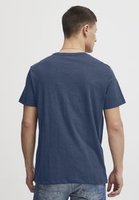 T-paita tummansinisellä värillä, lyhyillä hihoilla, pyöreällä pääntiellä ja pehmeällä pinnalla. Takaa nähtynä rento istuvuus ja yksinkertainen muotoilu ilman logoja.