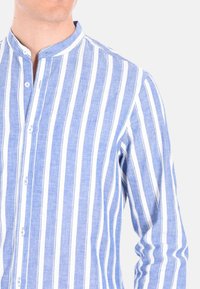 Camicia button-up a righe blu chiaro e bianche con colletto alla mandarino, realizzata in un tessuto testurizzato. Presenta bottoni bianchi e una vestibilità rilassata.