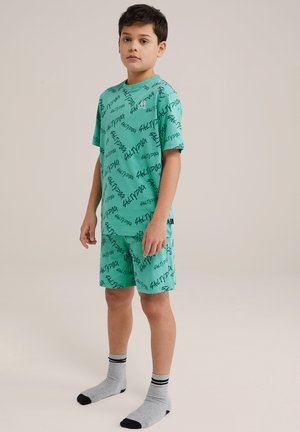 Turkos pyjamasset med svart textmönster, kort ärm och shorts, tillsammans med grå strumpor med svarta ränder upptill.