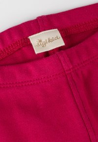 Nahaufnahme eines lebhaften pinkfarbenen Stoffes, der an der Taille ein angenähtes Etikett mit "sigikid" in goldener Schrift trägt.