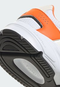 Baskets blanches avec des accents orange et noir. Matériaux en maille texturée et synthétiques. Étiquette Cloudfoam sur la semelle. Motif de traction en caoutchouc.