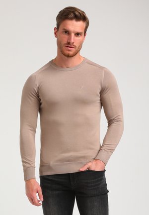 Beige pitkähihaine neulepaita, jossa on pyöreä pääntie, ribbaus hihansuissa ja helmassa, ja rinnassa pieni logo. Silitys, neulottu pinta.
