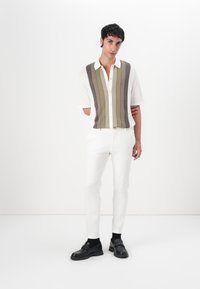 Kurzärmliges, kragenloses Hemd mit vertikalen Streifen in Grün und Braun, kombiniert mit schlanken weißen Hosen und schwarzen Schuhen. Minimalistisches Design.