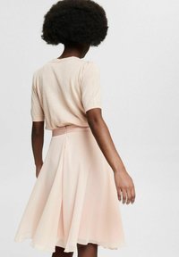 Lyserød kjole med tætsiddende overdel og udvidet nederdel, lavet af letvægtsstof. Har lynlås bagpå og korte ærmer.