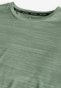 Grøn atletisk t-shirt med rund hals, lavet af tekstureret stof. Har en sort indre halsbånd med "ACTIVE" branding.