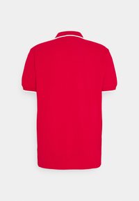 Polo rouge avec un col classique, des manches courtes et une bordure blanche le long du col et des manches. Texture de tissu lisse.