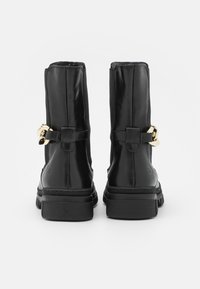 Bottines en cuir noir avec une semelle épaisse, ornées d'accents en métal doré et d'une sangle décorative. Texture lisse avec un design élégant.