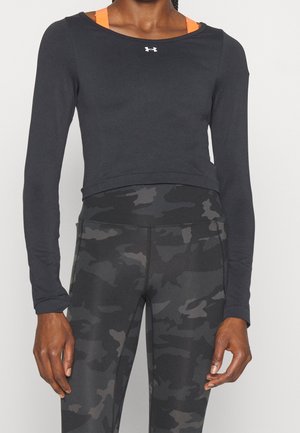 Osoba nosząca czarny krótki top z długim rękawem na pomarańczowym sportowym staniku oraz czarno-szare legginsy w kamuflaż o wysokim stanie.