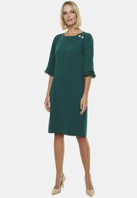 Zielona sukienka do kolan z krótkimi, falbaniastymi rękawami, okrągłym dekoltem i ozdobnymi guzikami w okolicy ramienia; gładki, sztywny materiał.