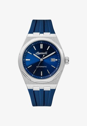 Zegarek automatyczny Ingersoll z ciemnoniebieską tarczą, srebrną stalową kopertą i niebieskim gumowym paskiem. Posiada okno daty oraz srebrne indeksy godzinowe.