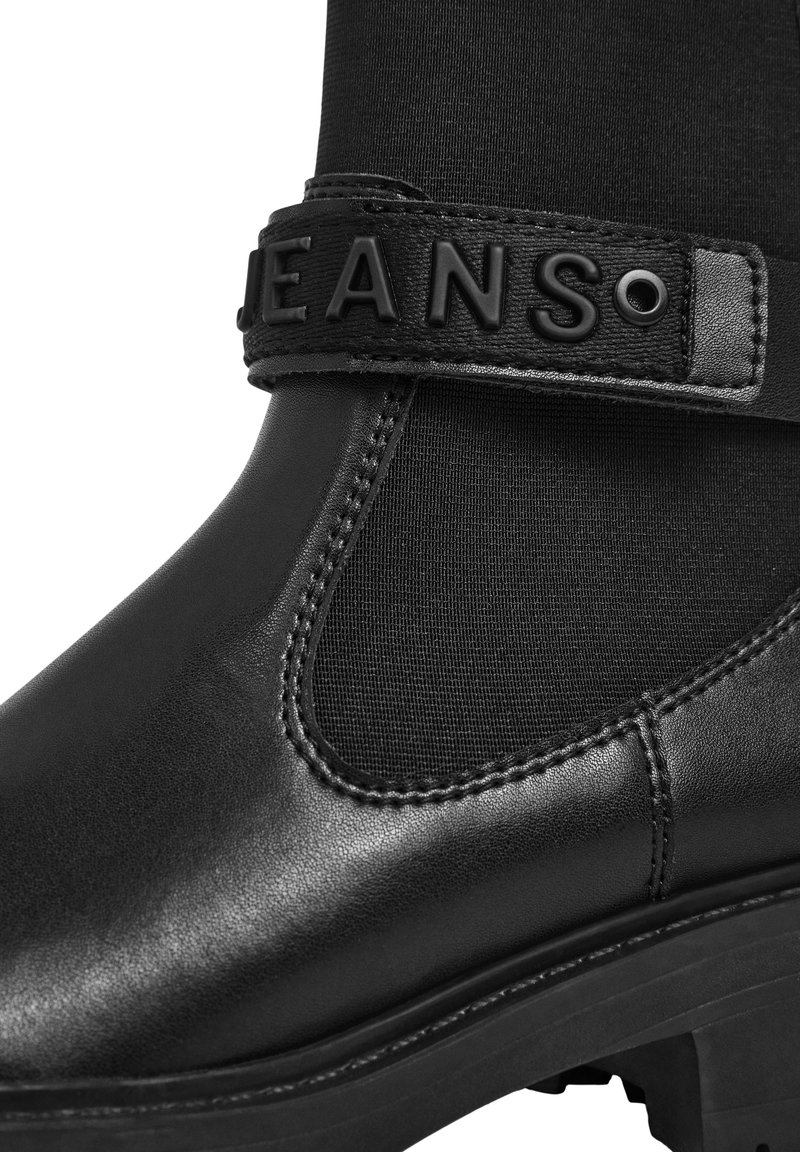 Stivale alla caviglia in pelle nera con pannello laterale elasticizzato e una fascia con lettere in rilievo "JEANS" in nero.