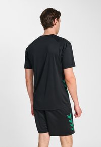 Czarny sportowy t-shirt z krótkim rękawem, z zielonymi akcentami w kształcie chevronów po bokach. Wykonany z lekkiego materiału, zaprojektowany z myślą o swobodzie ruchów.