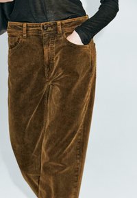 Pantalon en velours côtelé marron avec une surface texturée, coupe droite, passants de ceinture et poches latérales. Fermeture à bouton à la taille.