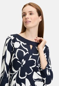 Navyblaues Langarmoberteil mit einem weißen Blumenmuster, V-förmigem Ausschnitt und glatter Textur sowie einer taillierten Silhouette.