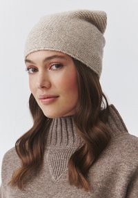 Beige neulotut myssy, jossa on kapeampi huippu; pehmeä rakenne. Yhdistetty kamelin väriseen ribbatuubikauluspaitaan, jossa on kolmiomainen yksityiskohta.
