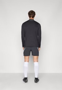 Svart långärmad sporttröja i kombination med grå shorts med sidodetaljer; vita knälånga strumpor och svarta fotbollsskor fulländar outfiten.