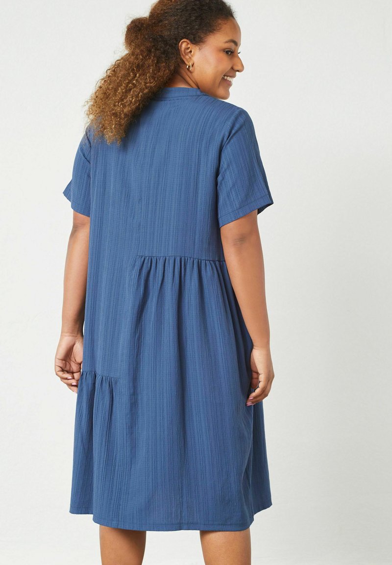 Blaues knielanges Kleid mit kurzen Ärmeln, strukturiertem Stoff, definiertem Taillenbereich und gerafftem Rockdetail. Die Rückansicht zeigt ein Nahtdesign.