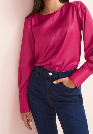 Blouse en satin fuchsia avec un col rond et des manches longues bouffantes, associée à un jean en denim bleu foncé avec une poche avant.