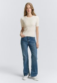 Crème ribbel korte mouwen top met een V-vormig ontwerp, gecombineerd met flare blue denim jeans en witte sneakers. Eenvoudige, casual outfit.