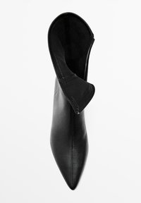 Stivale ankle in pelle nera con punta affilata e bordo piegato, caratterizzato da una superficie liscia e cuciture visibili lungo il bordo.