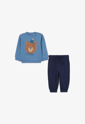 Sudadera azul de manga larga con un gráfico de un oso y texto, combinada con pantalones de forro polar azul marino con cintura elástica.