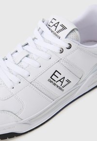 Bijela tenisica na vezanje s EA7 Emporio Armani logotipom na jeziku i bočnoj strani, perforiranim detaljima i crnim akcentima na potplatu.